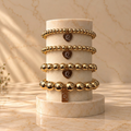 Four 18K gold-filled bracelets with Queenie Q heart and square tags stacked on a marble pedestal